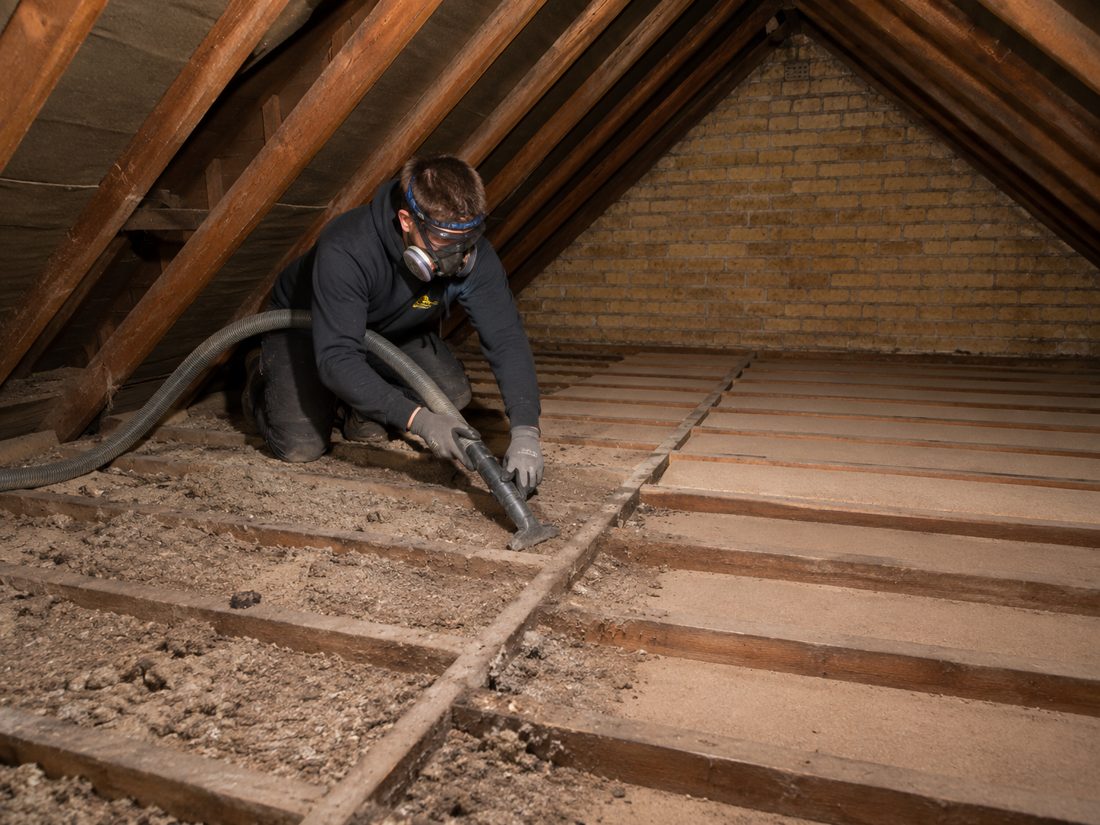 Old loft insulation and debris being vacuumed out from between the joists